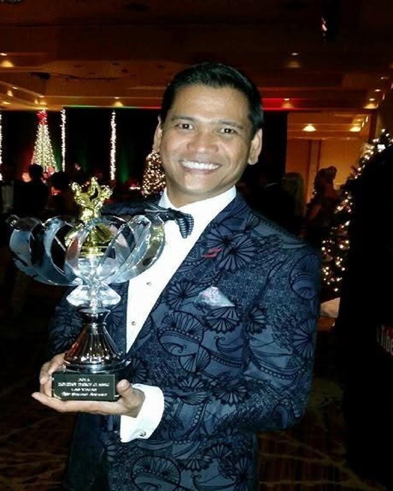 Allan Alday in a black suit holding a dance award trophy